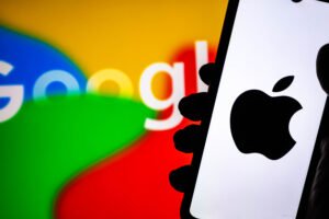 NADA NEWS hand holding a smartphone displaying the apple logo with the google logo blurred in the background